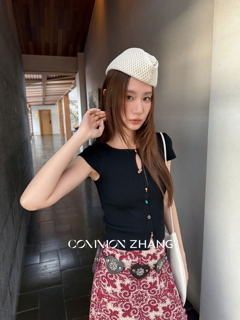 Woman wearing a black sleeveless top and patterned skirt with a white hat