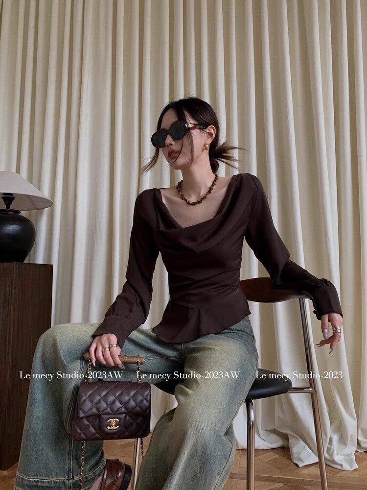 Model wearing a dark brown long-sleeve draped blouse with jeans and a handbag