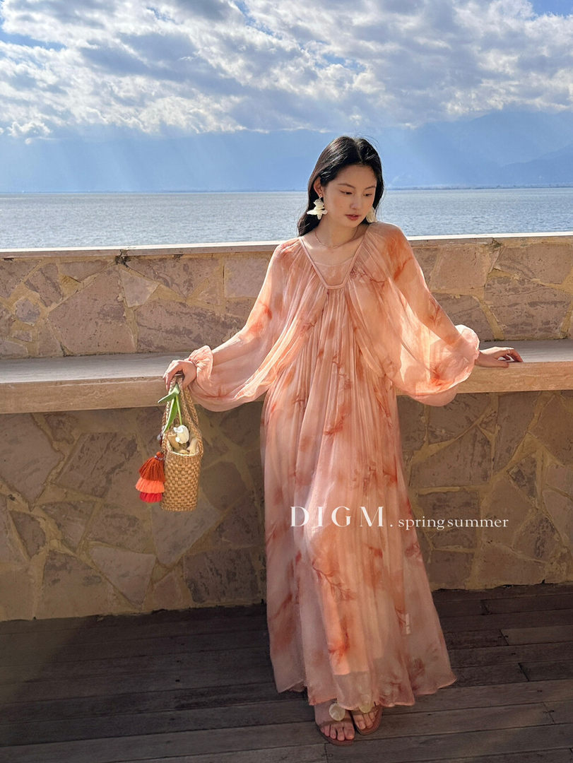 Model wearing a flowing peach sheer maxi dress by the sea