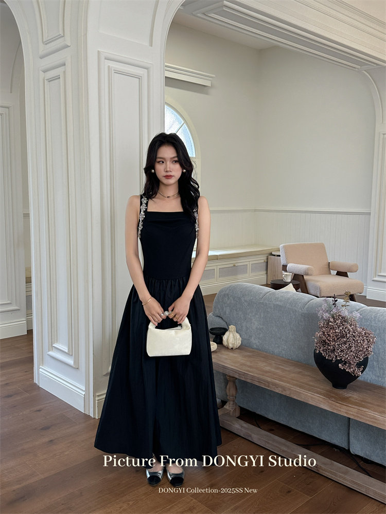 Black sleeveless maxi dress worn by a model holding a small white handbag
