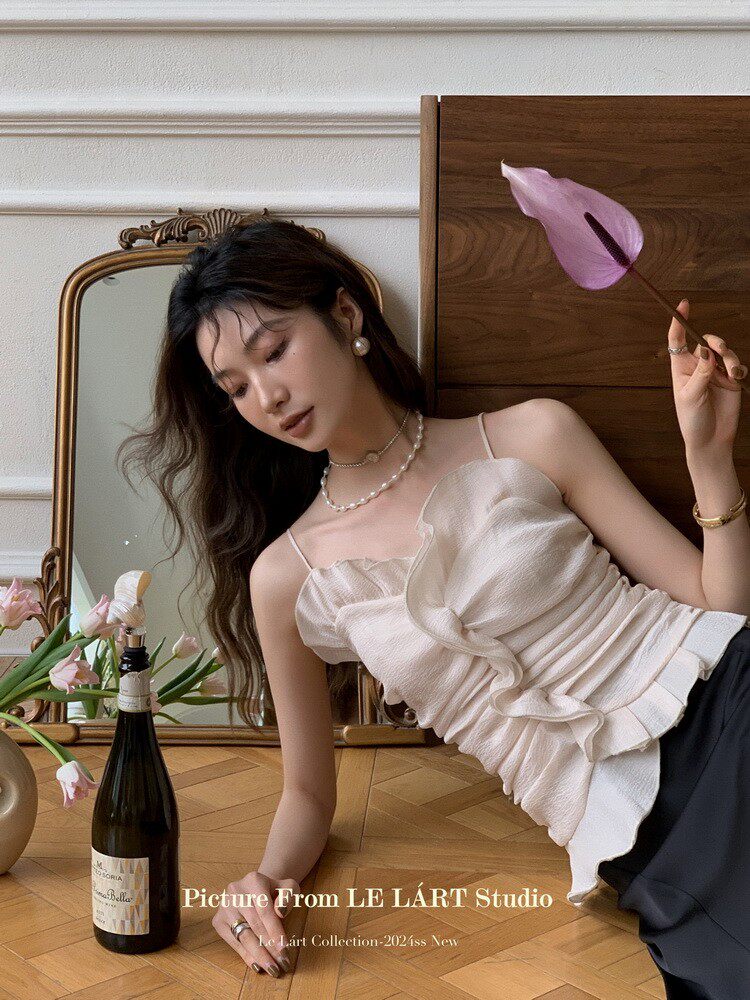 Model wearing a cream ruffled spaghetti-strap top with black pants