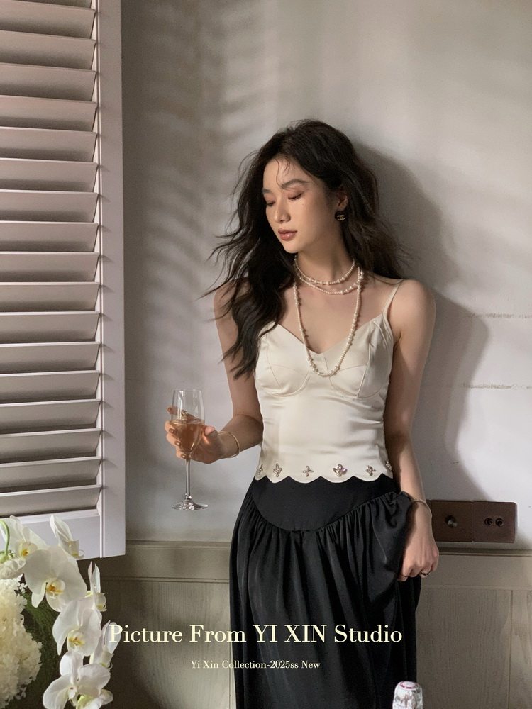 Woman wearing a cream camisole top with a black skirt in a studio setting
