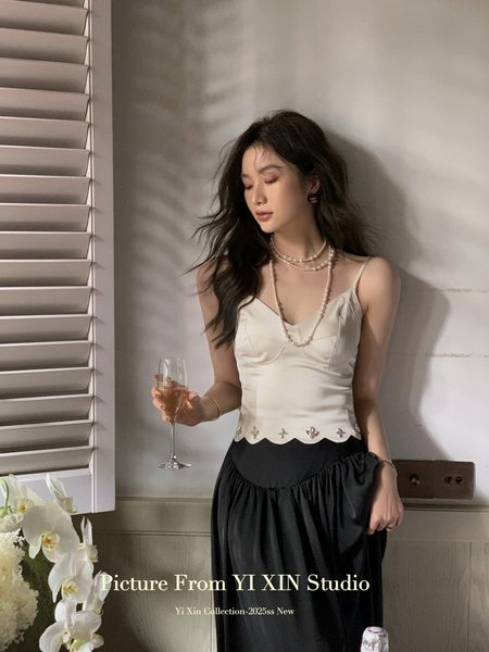 Woman wearing a cream camisole top with a black skirt in a studio setting