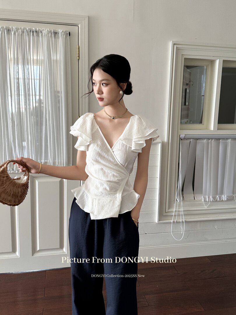 Model wearing a white ruffled wrap blouse with dark wide-leg pants