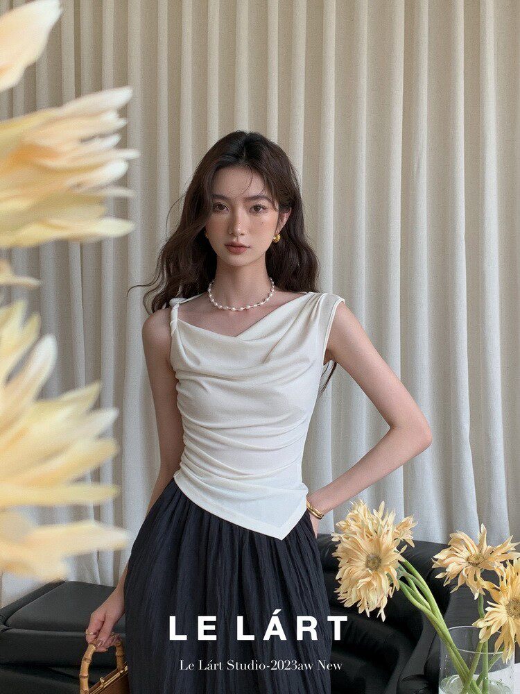 Model wearing a white draped sleeveless top with a dark skirt in a studio setting