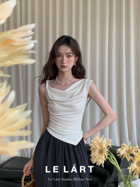 Model wearing a white draped sleeveless top with a dark skirt in a studio setting
