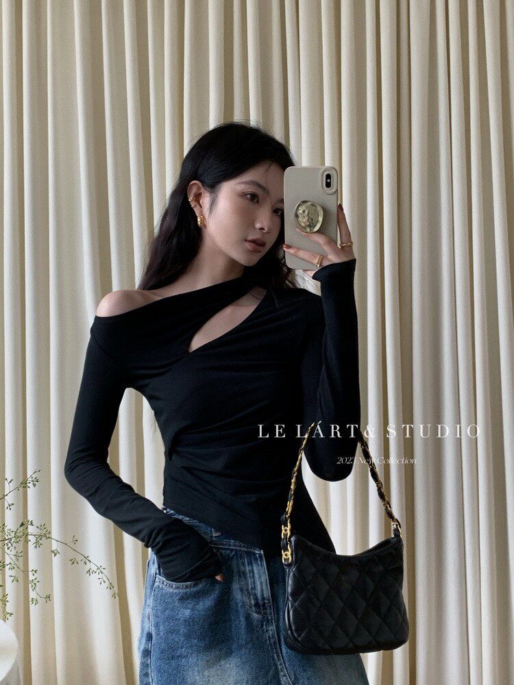 Model wearing a black asymmetrical off-shoulder top with jeans and a quilted black shoulder bag