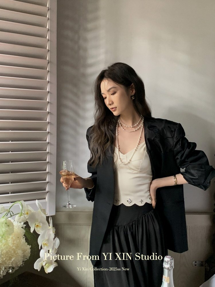 Woman wearing a black blazer over a cream top and black skirt