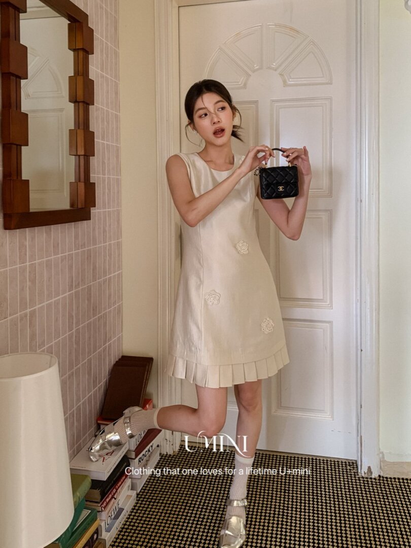 Cream sleeveless mini dress worn by a model with a small black handbag