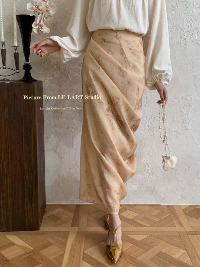 Model wearing a cream blouse with a beige draped satin skirt and gold heels