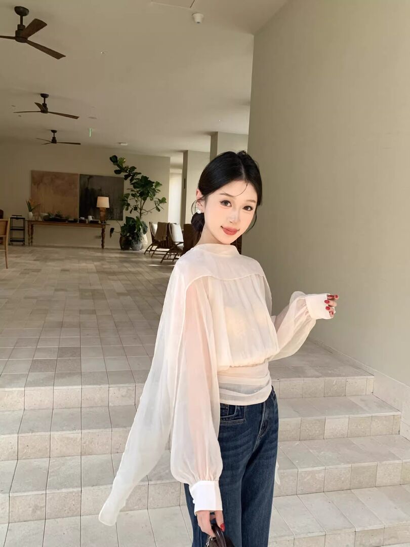 Model wearing a white sheer long-sleeve blouse with wide cuffs and dark jeans