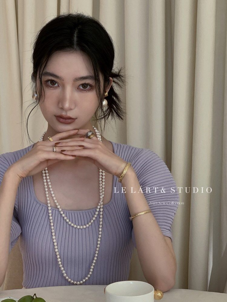Model wearing a lavender ribbed top with pearl necklaces and gold jewelry