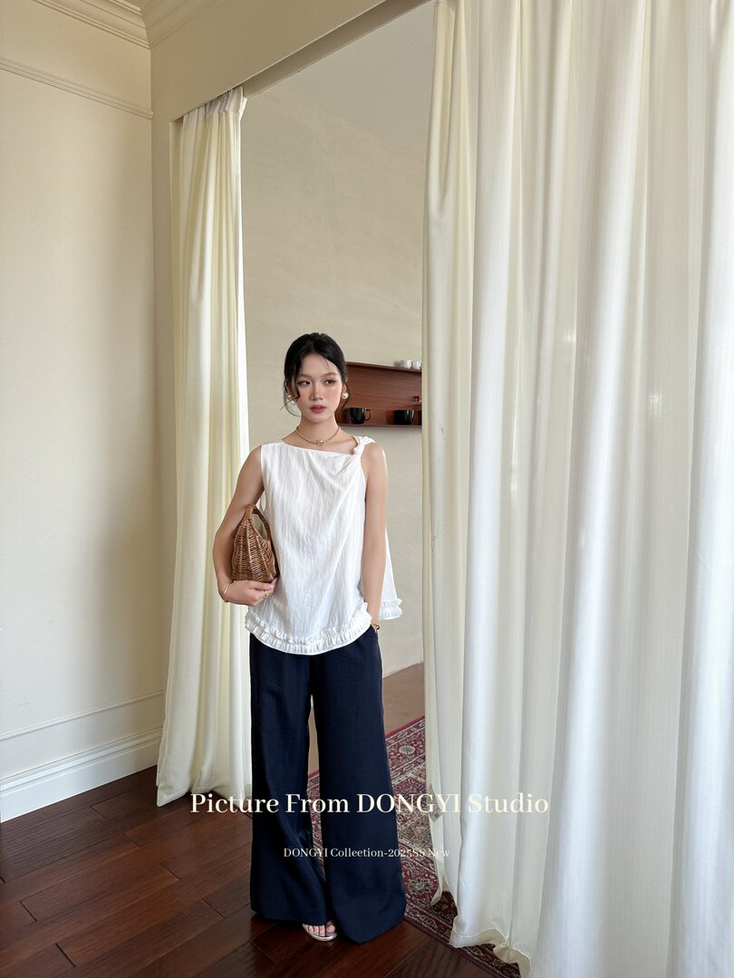 Model wearing a white sleeveless ruffled top with navy wide-leg pants