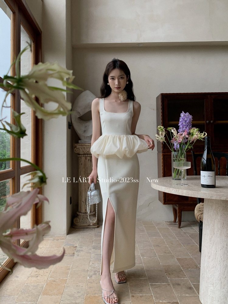 White sleeveless fitted midi dress with bubble peplum waist and thigh slit worn by a model