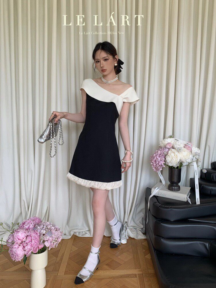 Model wearing a black and white off-shoulder mini dress with pearl accessories