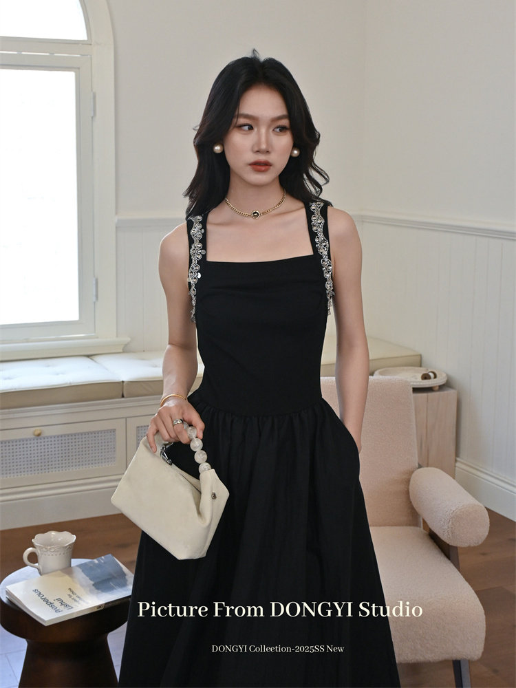 Black sleeveless dress worn by a model, holding a cream handbag