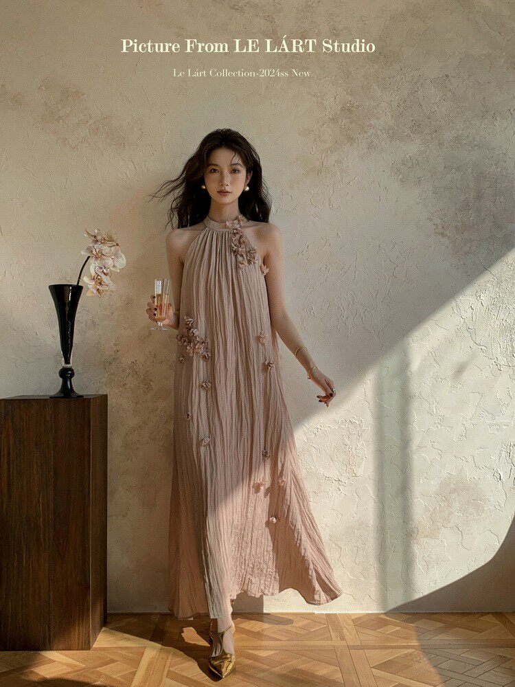 Model wearing a beige pleated halter maxi dress with floral embellishments