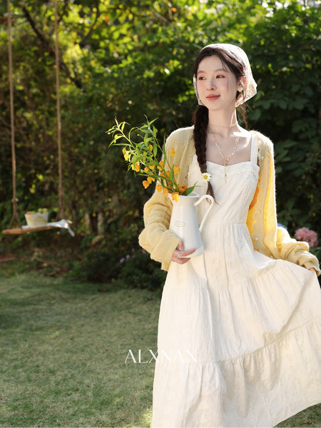 Woman wearing a white tiered dress with a yellow cardigan in a garden