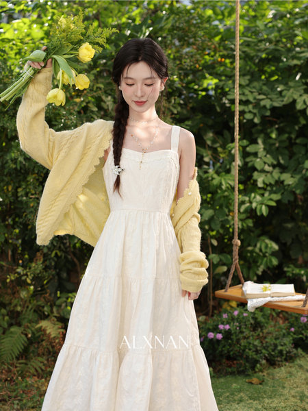 Model wearing a white sleeveless dress with a pale yellow cardigan outdoors