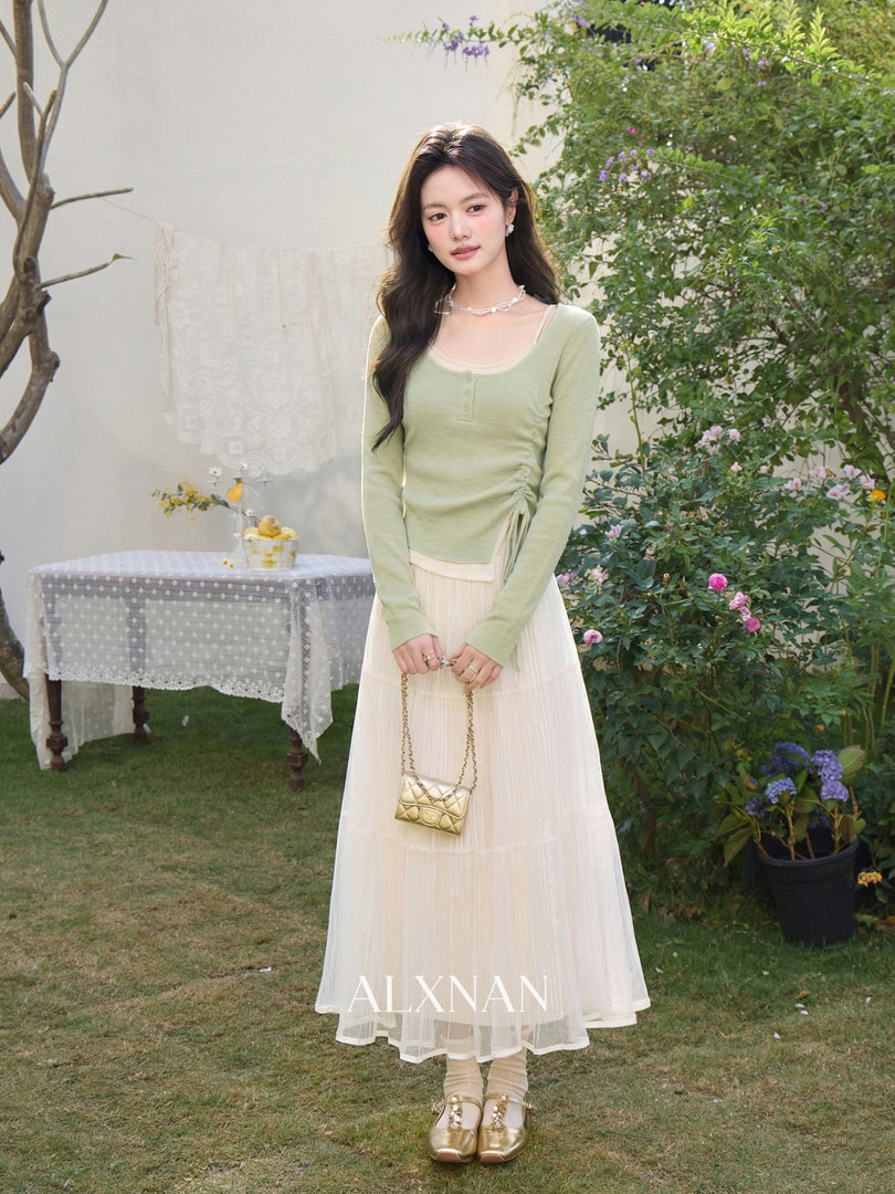 Model wearing a light green fitted top with a cream pleated midi skirt and gold mini bag