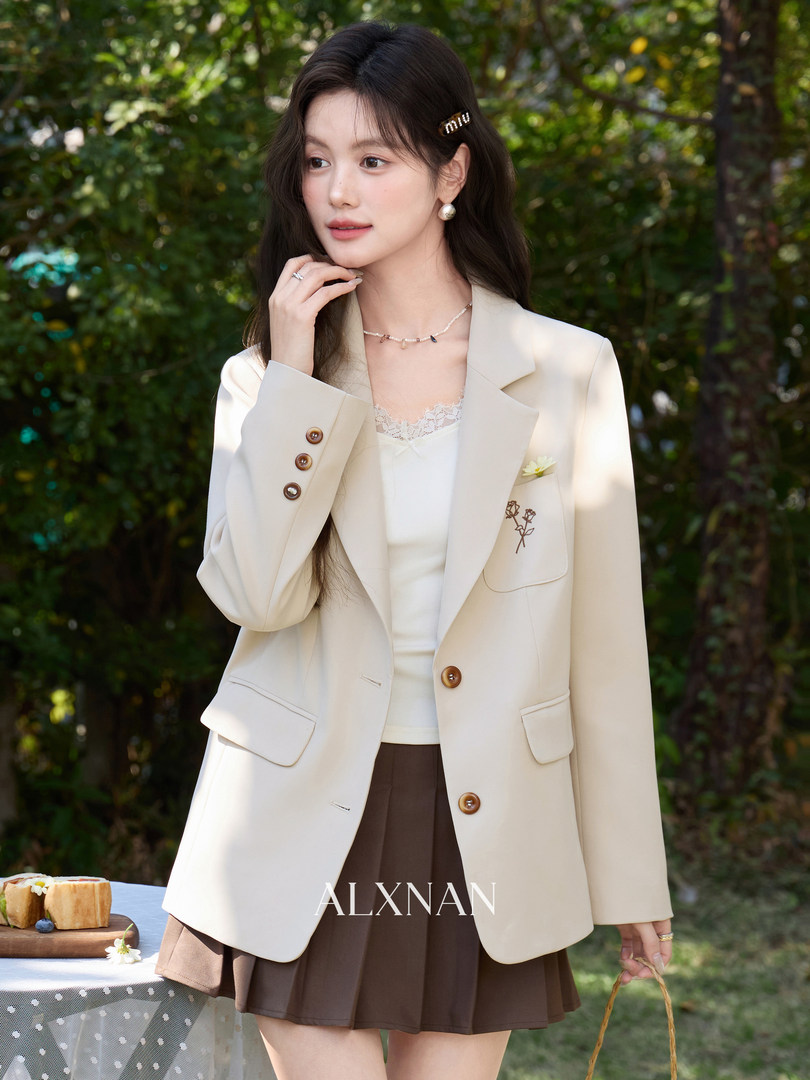 Woman wearing a cream blazer and brown pleated skirt outdoors