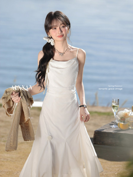 Model wearing a white satin dress outdoors by the sea