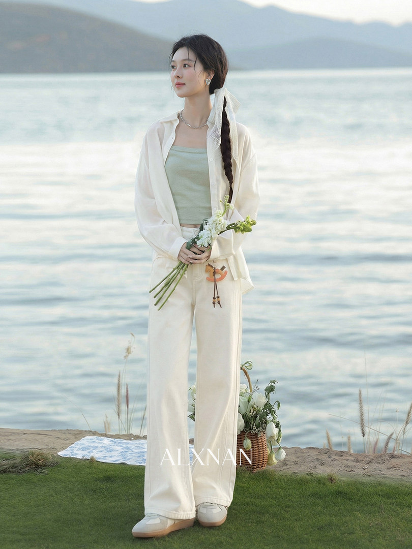 Woman wearing a light white shirt, crop top, and wide-leg pants by the water