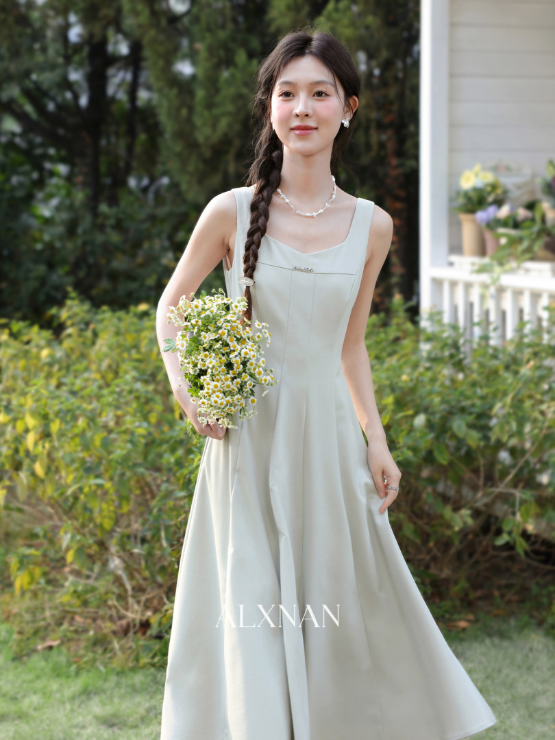 A model wearing a light-colored sleeveless formal maxi dress outdoors while holding a bouquet