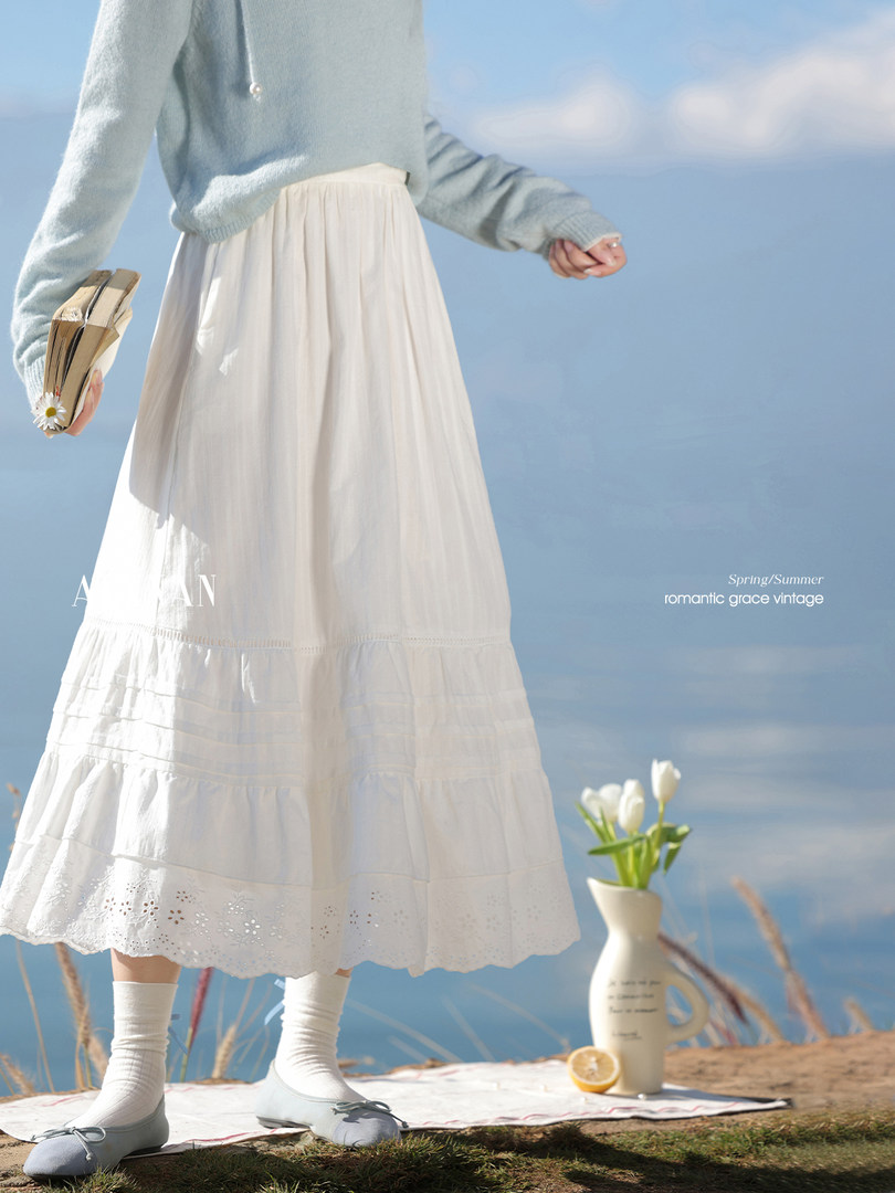 Woman wearing a white tiered maxi skirt with a light blue sweater by the sea