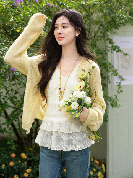 Woman wearing a pale yellow cardigan over a lace top while holding a bouquet outdoors