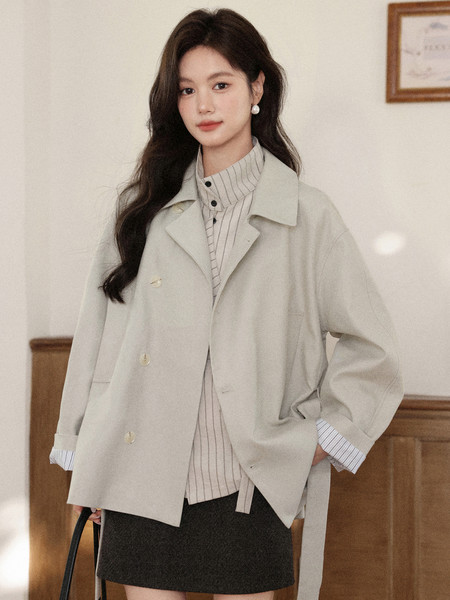 Woman wearing a light beige jacket over a striped shirt and dark skirt