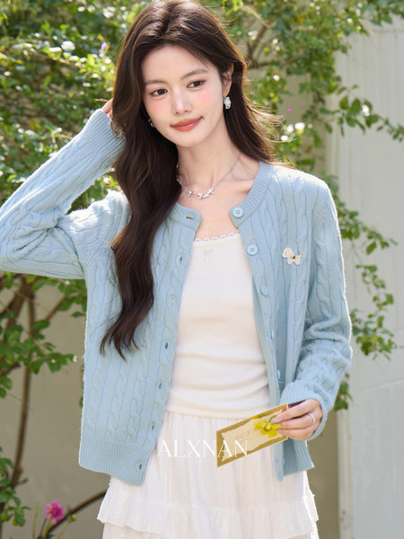 Light blue cable-knit cardigan worn over a white dress on a model outdoors
