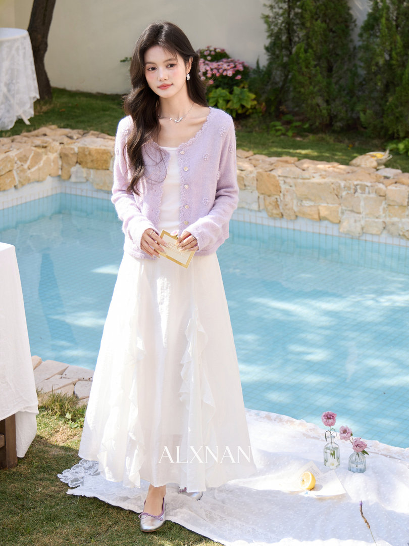 Model wearing a light lavender cardigan over a white dress outdoors by a pool