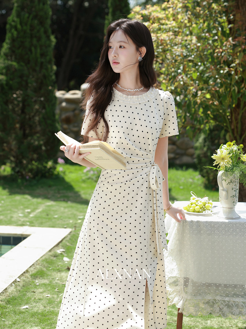 White polka dot wrap midi dress worn by a model outdoors in a garden