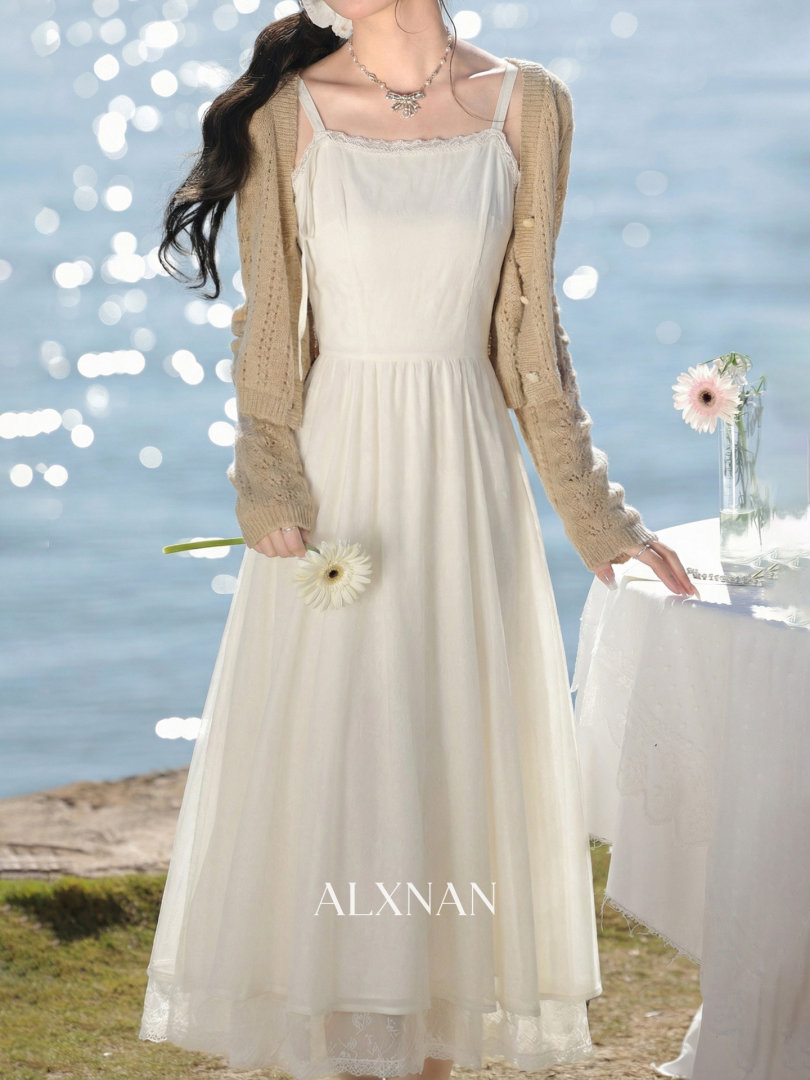 Model wearing a white slip dress with a beige knit cardigan by the seaside