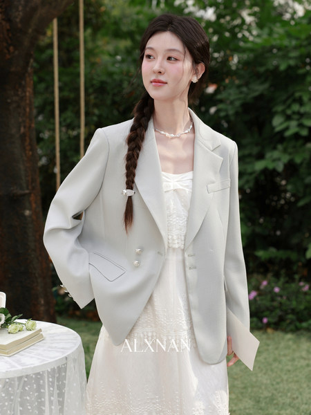 Woman wearing a light gray blazer over a white dress outdoors