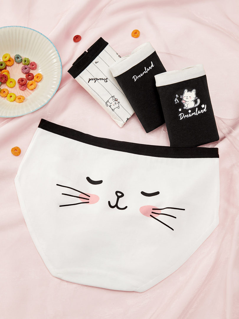 Cat-themed underwear briefs in black and white laid flat on a pink background