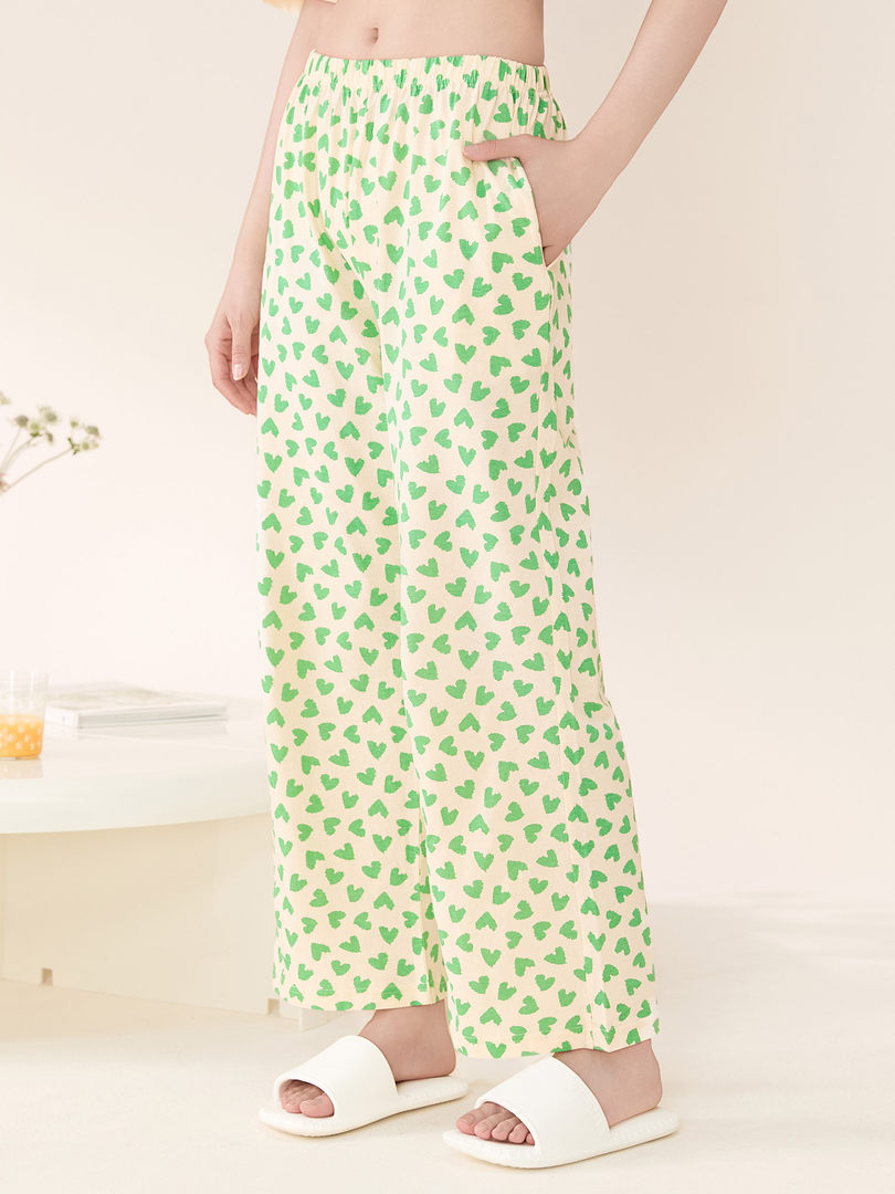 Model wearing cream lounge pants with green heart print and white slide sandals