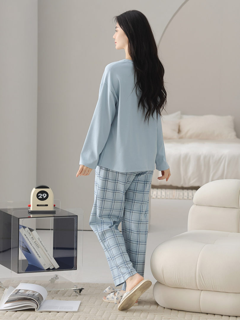 Woman wearing a light blue pajama set with plaid pants in a bedroom