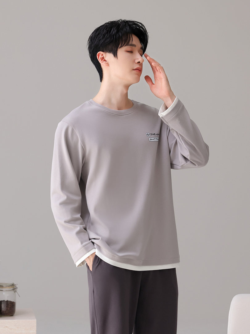 Man wearing a light gray long-sleeve crewneck shirt on a plain background