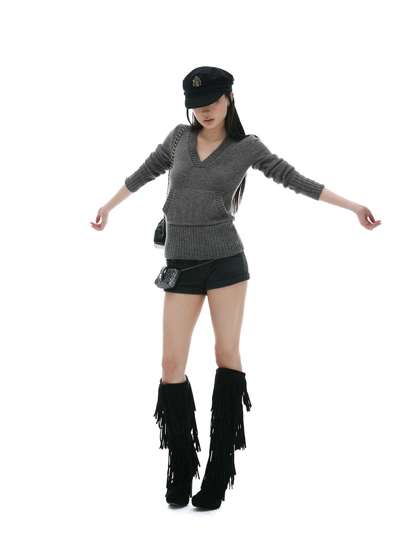 Fashion model wearing a gray knit sweater with black shorts and fringe boots on a white background