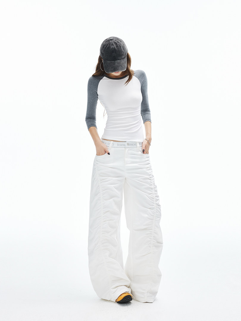 Model wearing a white wide-leg pant and gray-and-white long-sleeve top with a black cap