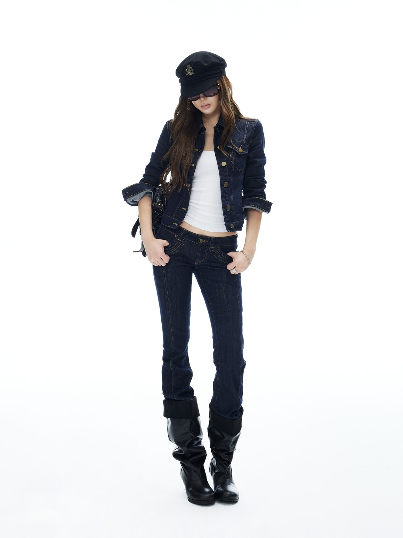 Woman wearing a dark denim jacket and jeans with a black hat and boots on a white background