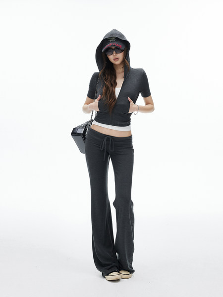 Model wearing a dark hooded zip-up top and flared pants with a cap and sunglasses