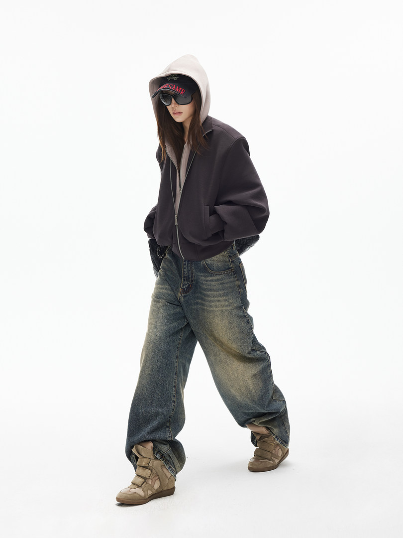 Model wearing a hooded jacket, wide-leg jeans, cap, sunglasses, and sneakers on a white background