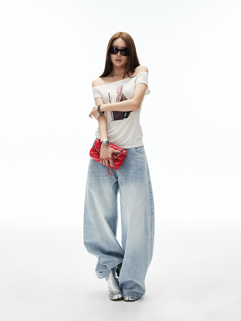 Model wearing a white off-shoulder top, wide-leg jeans, and a red handbag