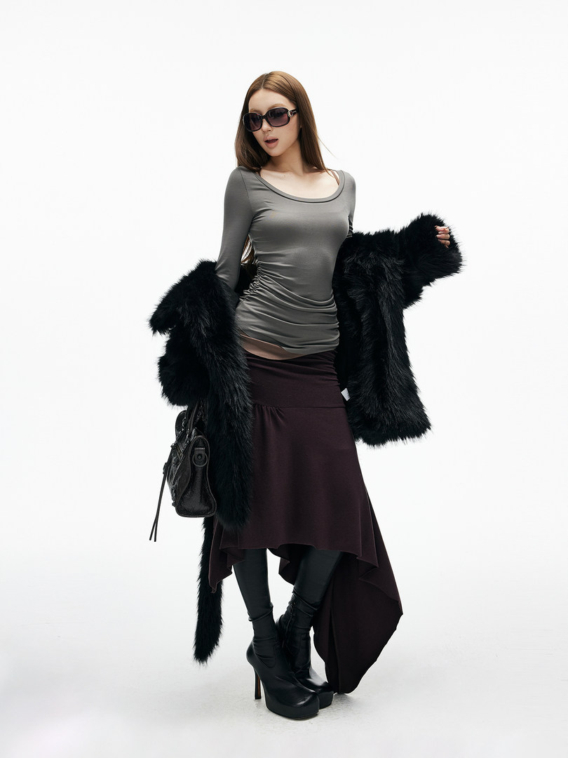 Fashion model wearing a gray top, dark skirt, black fur coat, and black boots
