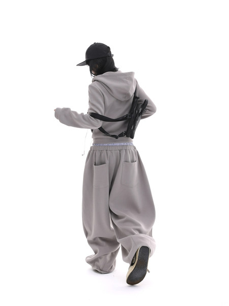 Model wearing a light gray hoodie and baggy pants with a black cap and backpack