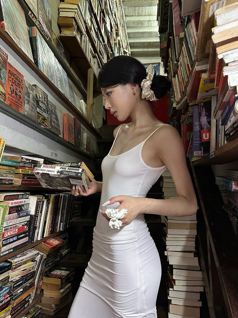 Woman wearing a white fitted sleeveless dress in a bookstore aisle
