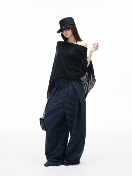 Fashion model wearing a black draped top, pinstripe wide-leg pants, and a black hat with sunglasses